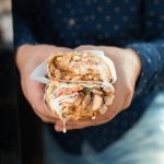 Delicious chicken shawarma held by hand, wrapped with fresh ingredients.