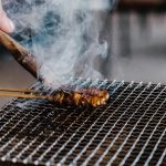 Close-up of juicy skewered meat grilling with smoke rising on a barbecue.