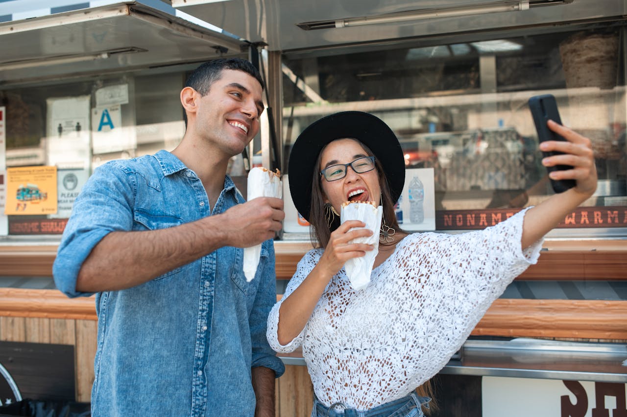 A joyful moment captured as friends take a selfie while enjoying food at a street food truck.