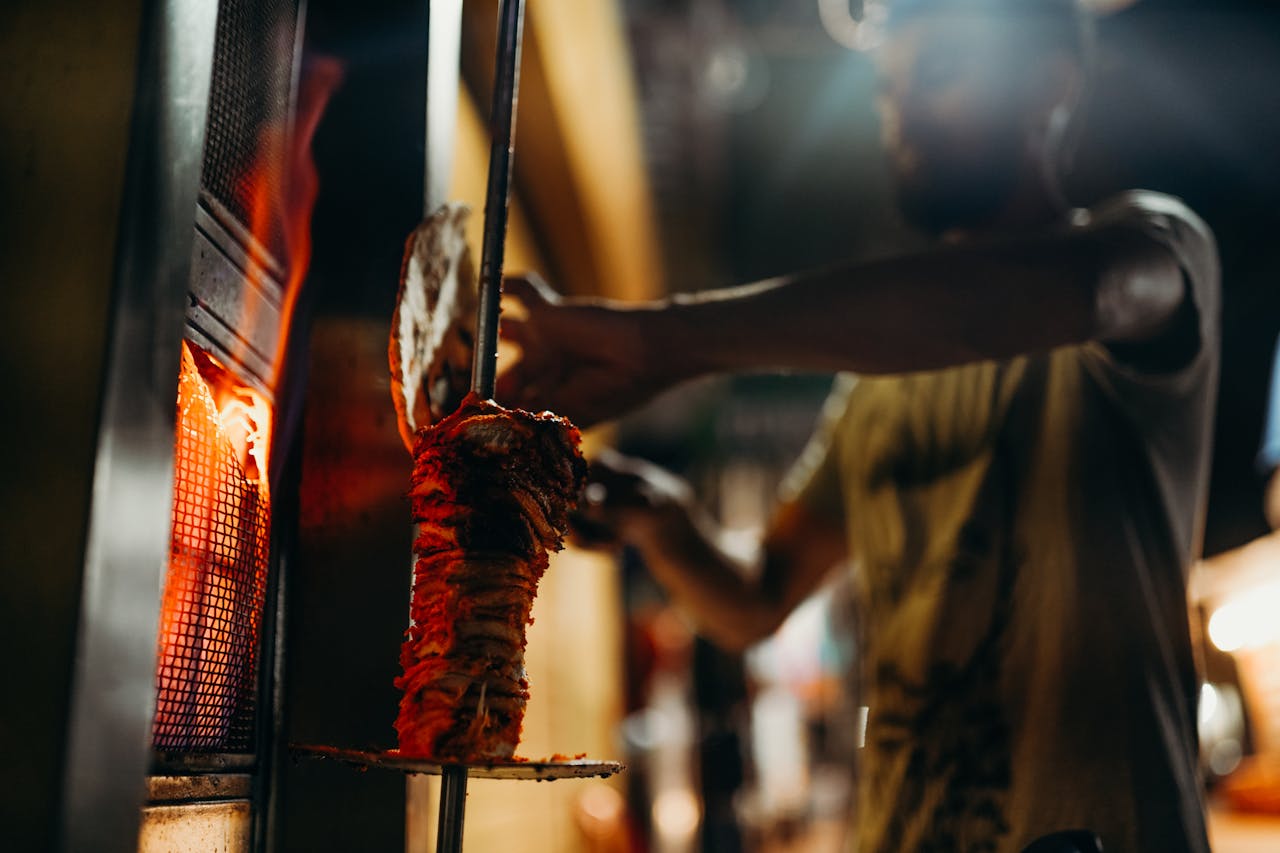 Close-up of a chef grilling shawarma on an open flame, showcasing traditional barbecue techniques.